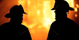 عکس با کیفیت دو آتش نشان در تاریکی در حال بررسی آتش با زمینه شعله های نارنجی و قرمز سوزان آتش مناسب برای روز آتش نشان و فروشگاه های تجهیزات آتش نشانی