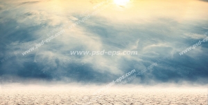 عکس با کیفیت بیابان خشک و زمین ترک خورده در آسمان نیمه ابری و با تلالو نور نارنجی خورشید