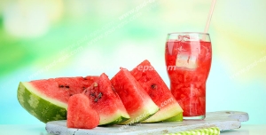 عکس با کیفیت لیوان آب هندوانه در کنار برش های هندوانه بر روی میز