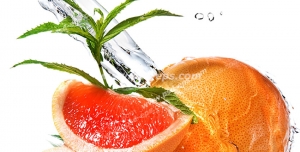 عکس با کیفیت برخورد آب با پرتقالی سالم و برشی از پرتقال خونی در کنار برگ های درخت پرتقال