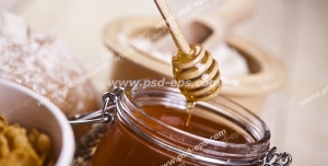 عکس با کیفیت شیشه عسل بر روی میز و برداشتن عسل از درون آن با قاشق مخصوص عسل