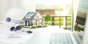 عکس با کیفیت تبلیغاتی لپ تاپ در کنار ماکت خانه کوچک و نقشه های لول شده ی ساختمان