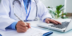 عکس با کیفیت تبلیغاتی دکتر در حال کار کردن با لپ تاپ و نوشتن وضعیت بیمار بر روی کاغذ