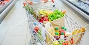 عکس با کیفیت تبلیغاتی سبد چرخدار فروشگاه در دست زن و سبد پر شده از سبزیجات و میوه و مواد غذایی